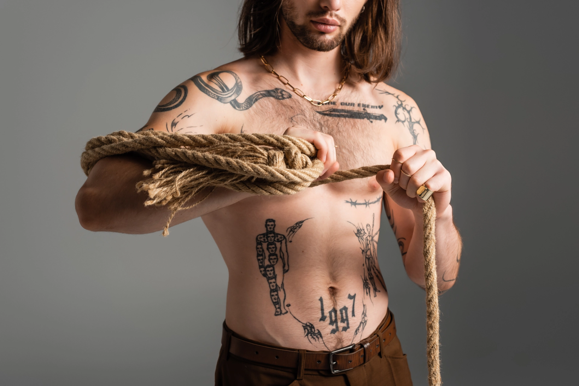 Long haired shirtless man with tattoos on his stomach, chest, and shoulders