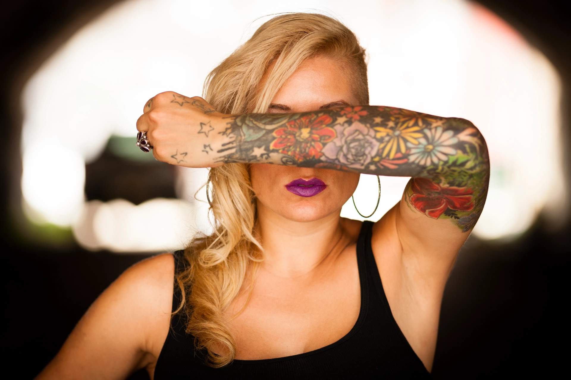 woman covering eyes with arm that has colorful tattoos