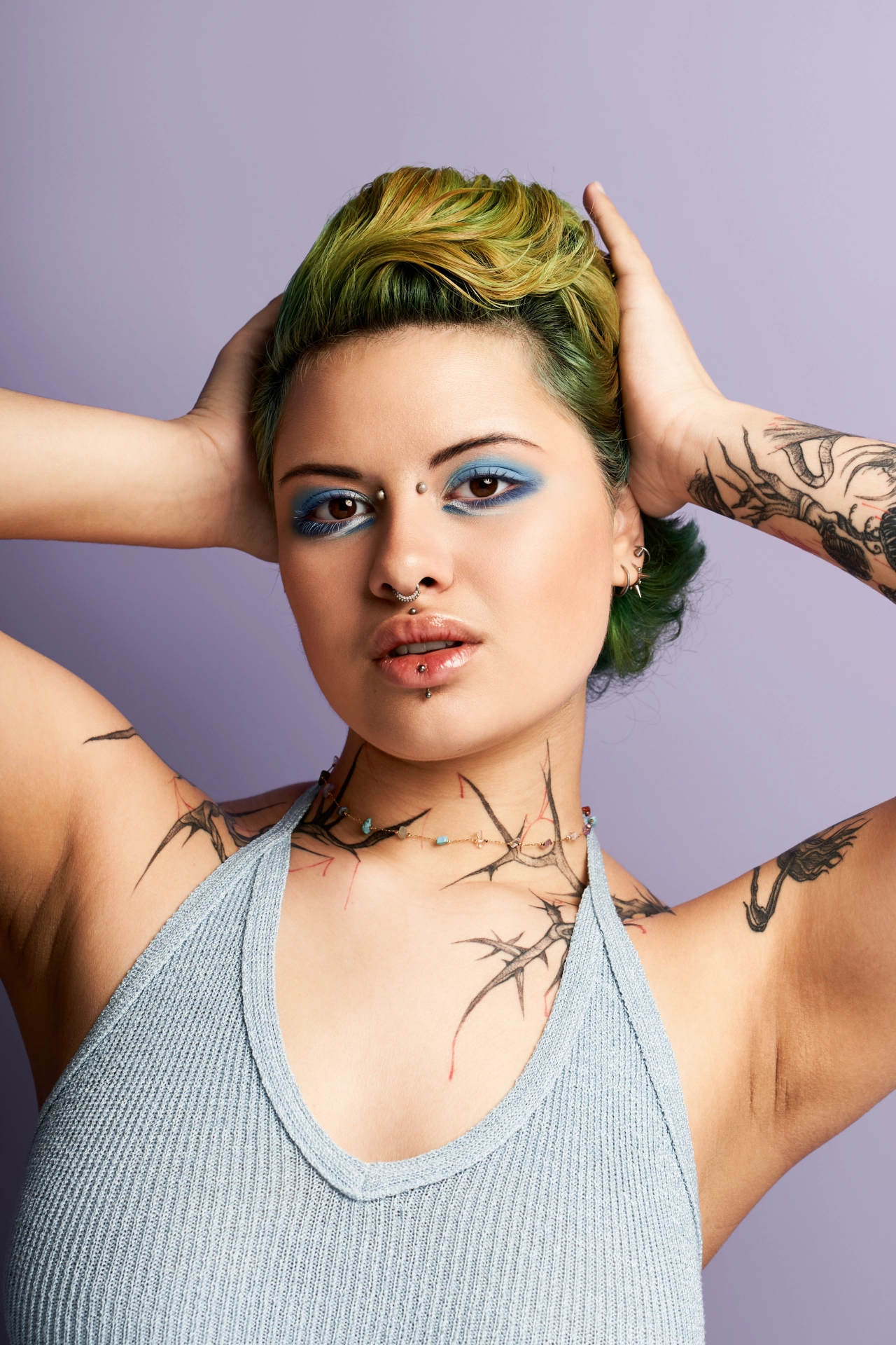 Woman with hands on head showing tattoos on shoulders and arm